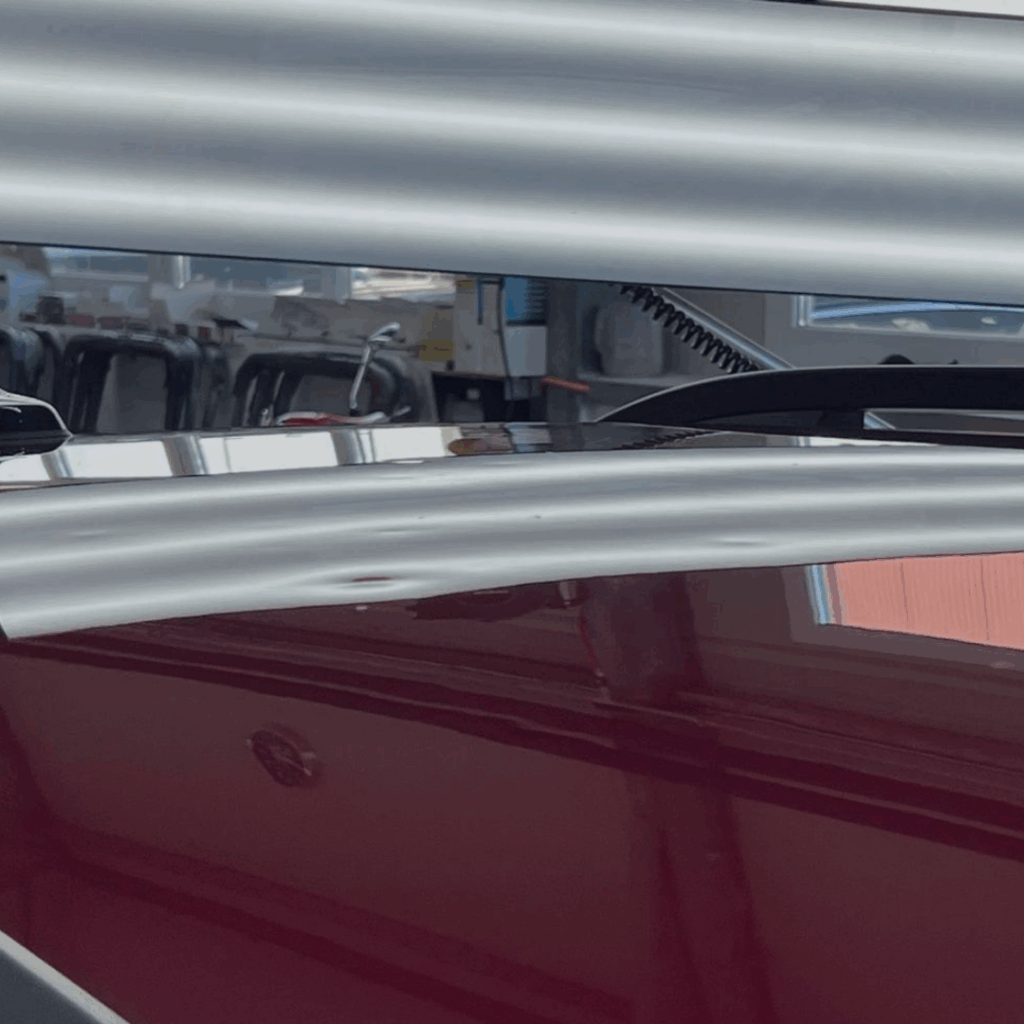 Inspection d’une carrosserie rouge avec lampe de contrôle lors d’un débosselage sans peinture à la Carrosserie du Relais SA à Sonceboz-Sombeval, Jura bernois.